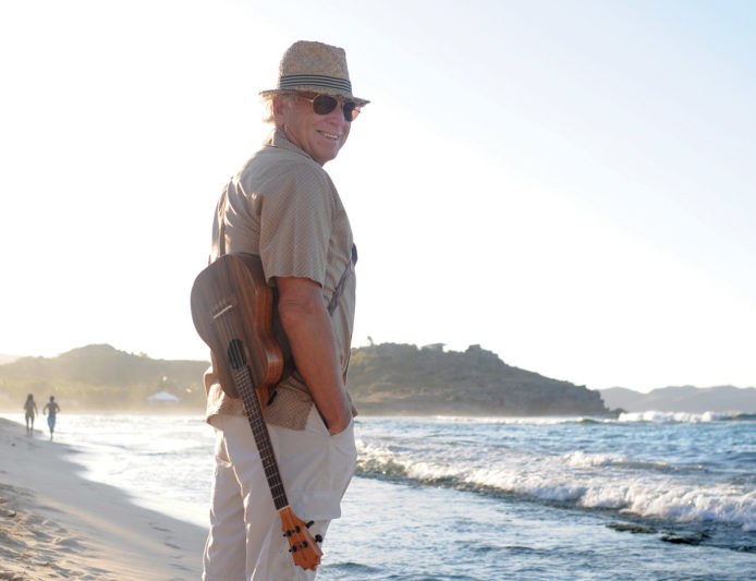 Jimmy Buffett walking on the beach at sunset with a ukulele